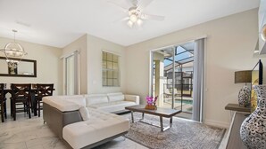A modern living room with a sofa, coffee table, and dining area. - Four Bedroom Close to Disney w Pool 4898 (Kissimmee)
