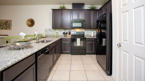 Uma cozinha moderna com armários escuros, bancada de granito, eletrodomésticos de aço inoxidável e backsplash revestido de azulejos.