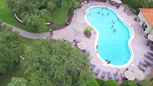 Vista aérea de uma área residencial com piscina, cercada por espreguiçadeiras e guarda-sóis, sugerindo um ambiente de resort ou hotel.