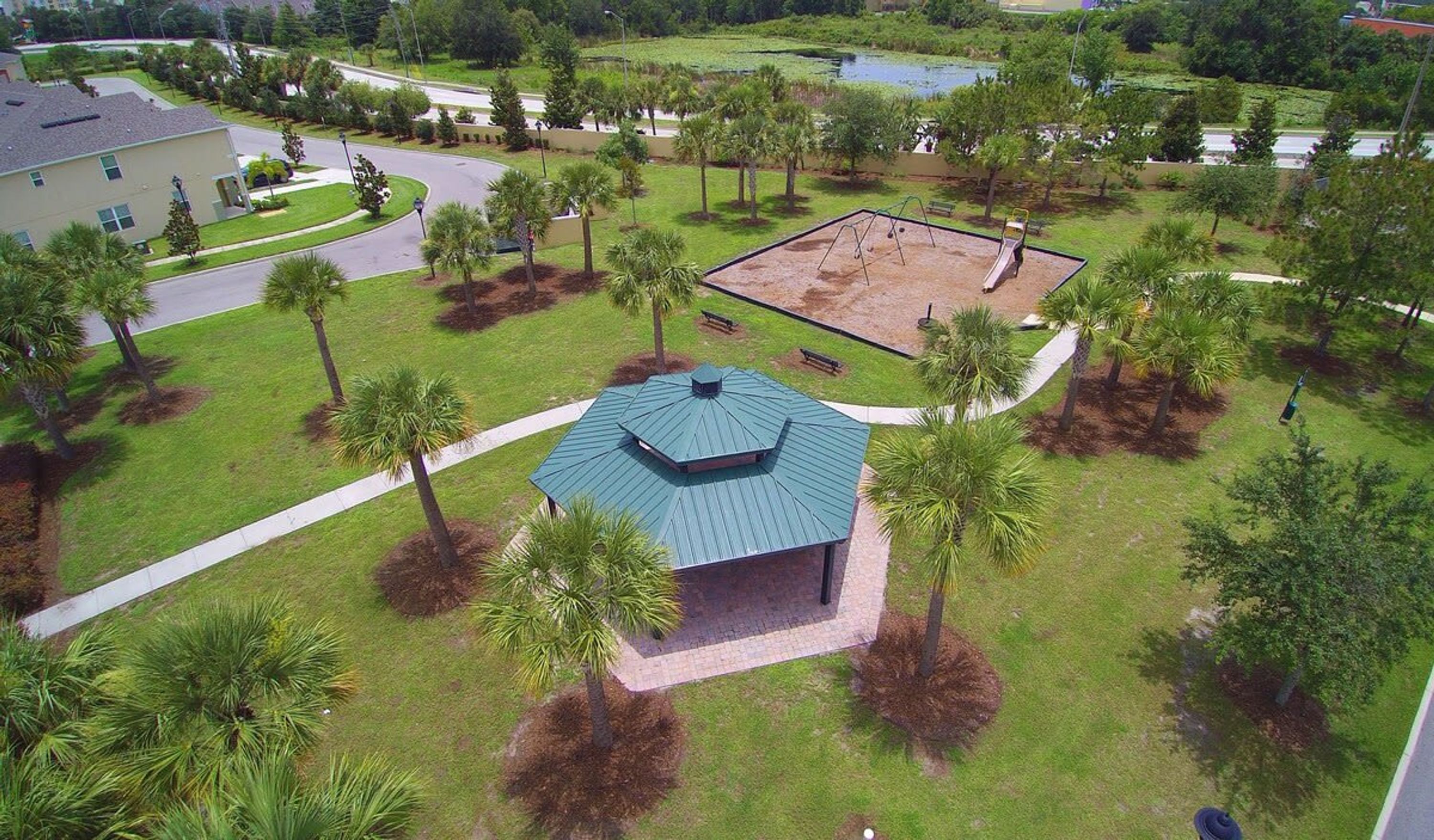 A building with a green roof surrounded by palm trees and a playground.