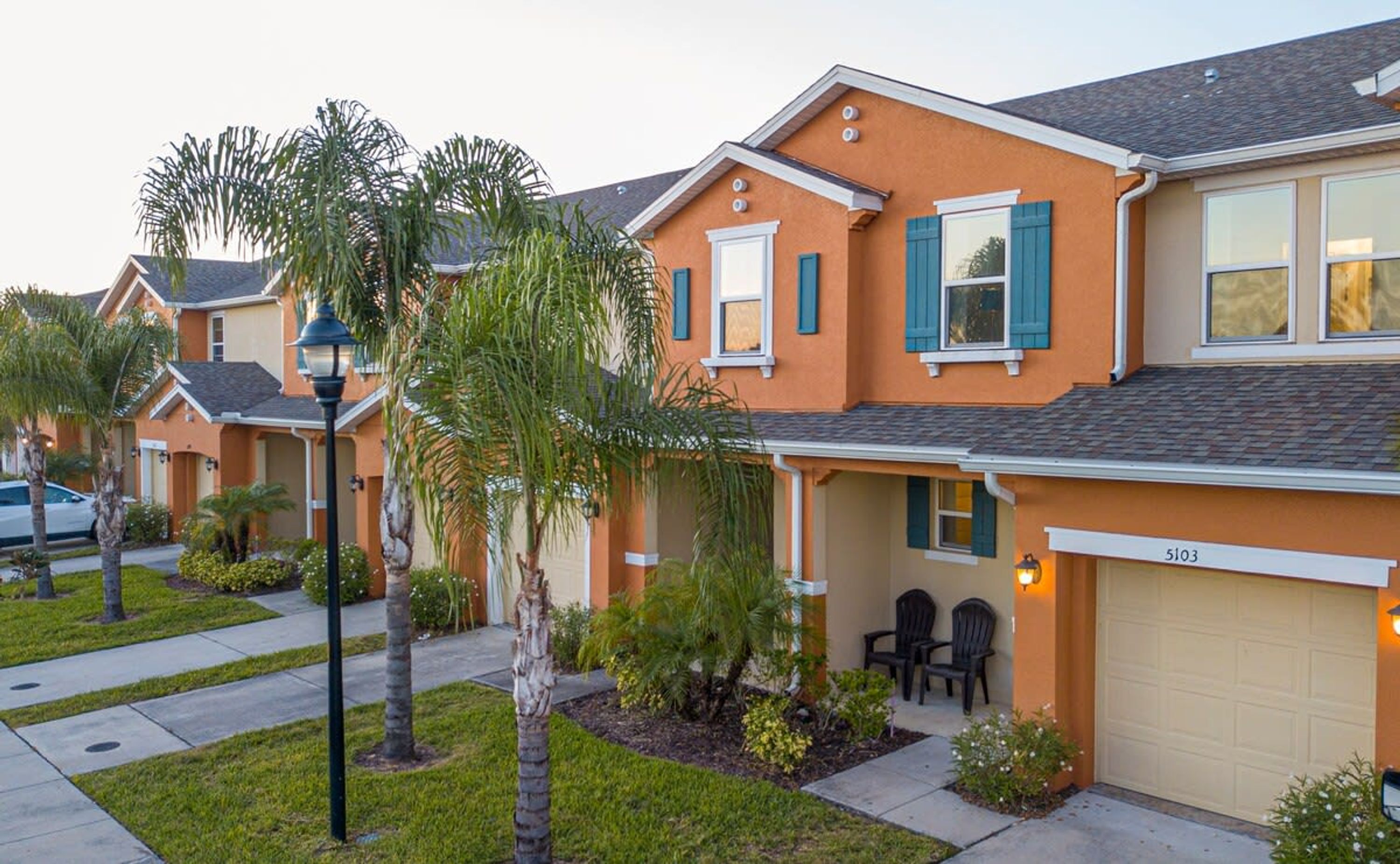 A row of townhouses with a garage, outdoor seating, and palm trees.