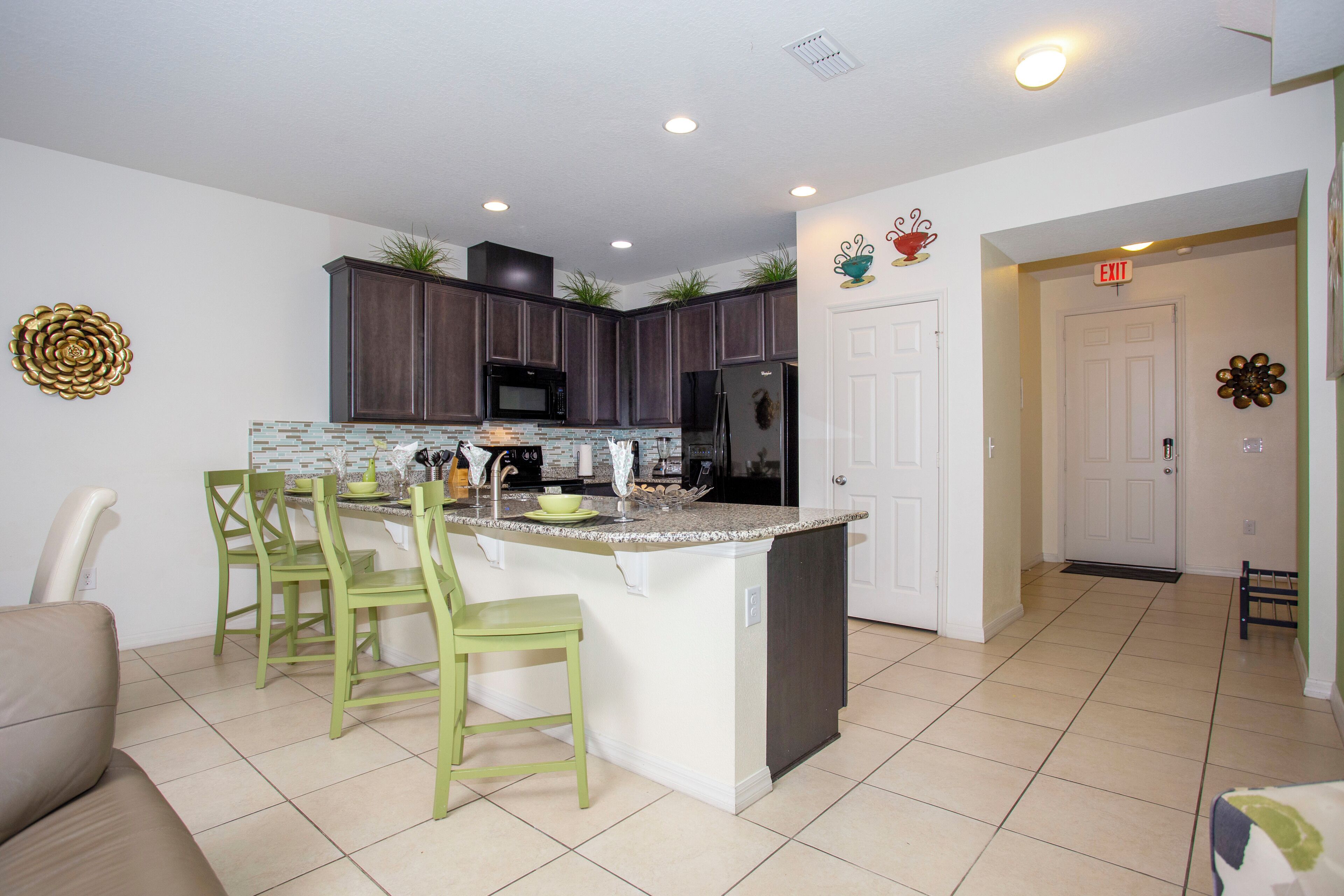 A modern kitchen with a central island, green chairs, and dark wooden cabinets.