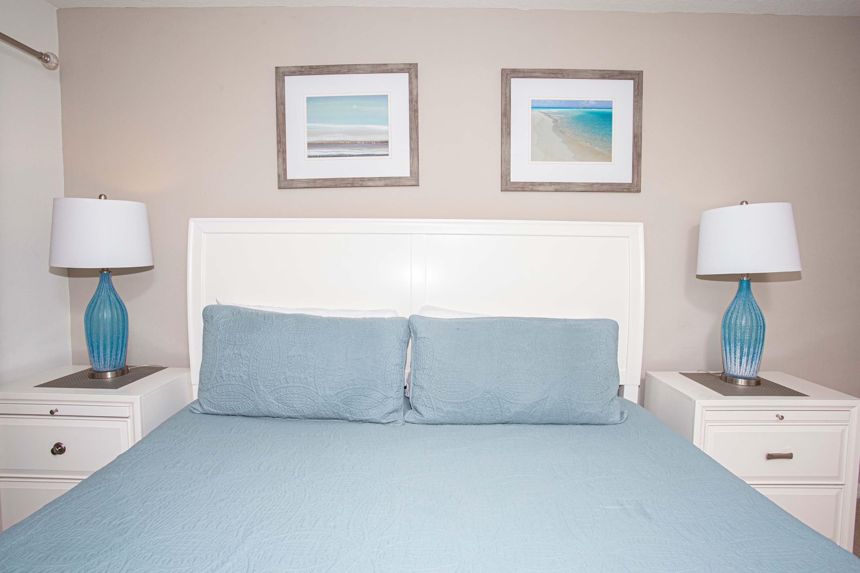 A bedroom with a bed, two nightstands, two lamps, and two framed pictures on the wall.
