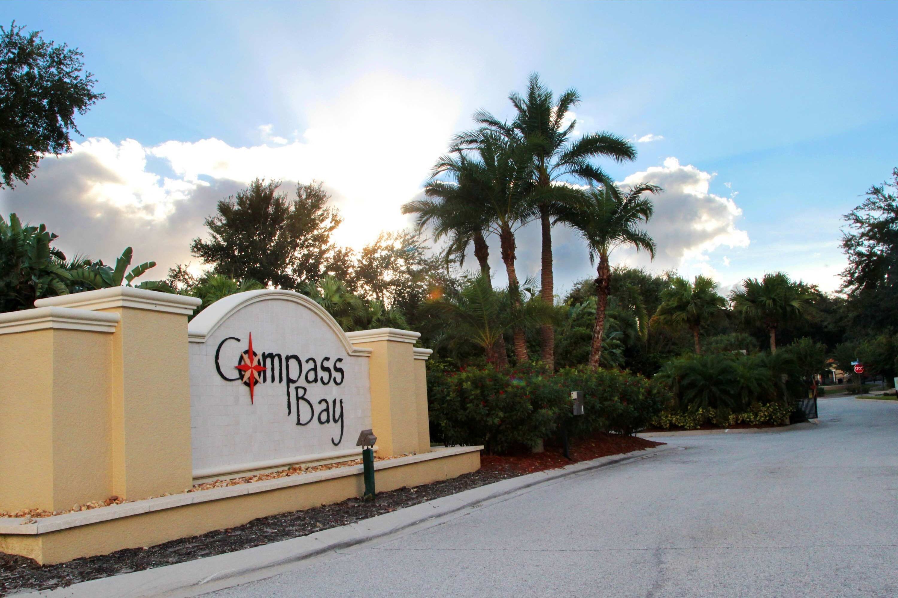 A sign for Compass Bay with a curved top and a star emblem, surrounded by palm trees and a clear sky.