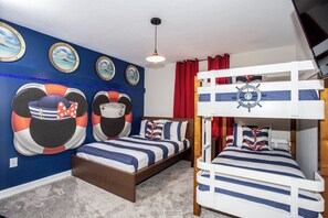 Un dormitorio con temática náutica, con literas, ropa de cama a rayas y decoraciones marítimas en las paredes.