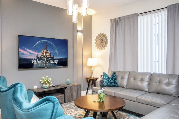Una sala de estar con una televisión de pantalla plana, un sofá, una mesa de centro y una lámpara.