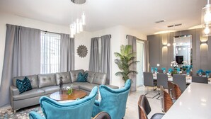 Una sala moderna con un sofá gris, sillones azules, una mesita de centro y un comedor con una mesa larga y sillas.