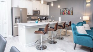 Una cocina moderna con armarios blancos, electrodomésticos de acero inoxidable y una isla central con taburetes de bar.