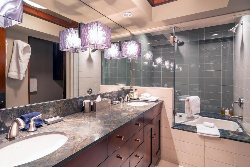 A modern bathroom with a large vanity, dual sinks, and a glass-enclosed shower.
