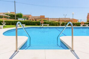 Une piscine aux eaux d’un bleu limpide, bordée d’une rambarde en métal, avec une bouée de sauvetage et un banc.