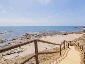 A wooden staircase leading to a rocky beach with a clear view of the ocean.