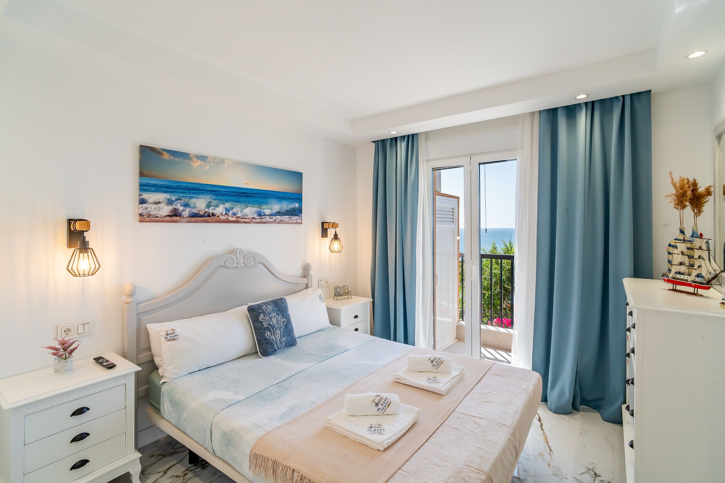 Un dormitorio con cama, mesitas de noche, un cuadro y vistas al exterior.