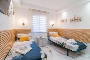 A bedroom with two beds, a nightstand, and wall-mounted light fixtures.