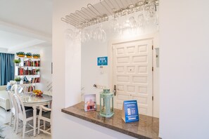 Un interior moderno con una mesa de comedor de vidrio, sillas blancas, una estantería y una puerta con un ojo de cerradura.