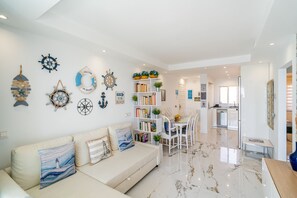 Un salon moderne comprenant un canapé, une table à manger avec des chaises, une bibliothèque et des éléments de décoration murale sur le thème de la marine.