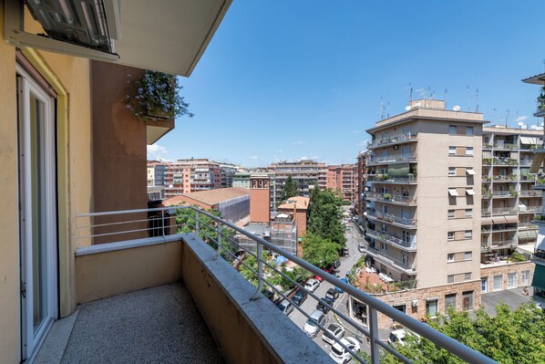 A balcony with a metal railing overlooking a cityscape with multi-story buildings and parked cars.