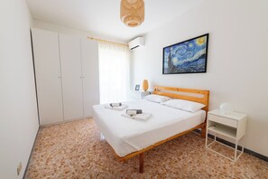 A bedroom with a bed, a bedside table, a wardrobe, a painting on the wall, and a window with curtains.