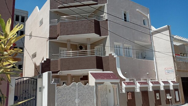 A multi-story residential building with a gated entrance, balconies, and a visible air conditioning unit. - Appartement HS à Bord de la mer Sousse Chott Meriam (Chott Meriam)