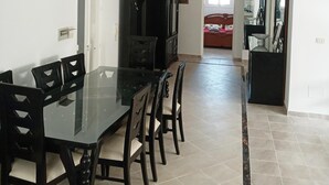 A dining area with a glass table and chairs, a black cabinet, and a chandelier. - Appartement HS à Bord de la mer Sousse Chott Meriam (Chott Meriam)