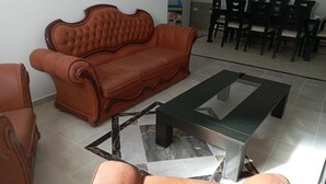 A living room with a brown sofa, a glass-top coffee table, and a dining area with black chairs. - Appartement HS à Bord de la mer Sousse Chott Meriam (Chott Meriam)