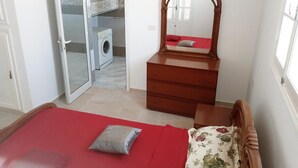 A bedroom with a bed, a dresser, a mirror, a wardrobe, and a washing machine in the background. - Appartement HS à Bord de la mer Sousse Chott Meriam (Chott Meriam)