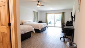 Ein Hotelzimmer mit zwei Betten, einem Schreibtisch, einem Computer und einem Deckenventilator.