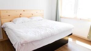Een bed met een houten hoofdbord, wit beddengoed en een raam met gordijnen.