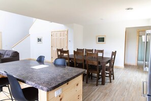 Een moderne keuken met granieten aanrechtbladen, houten keukenkastjes en een eethoek met een grote tafel en stoelen.