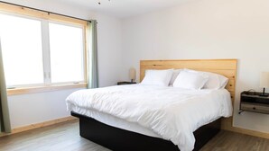 Une chambre à coucher avec un grand lit, une tête de lit en bois, une table de chevet avec une lampe et une fenêtre avec des rideaux.