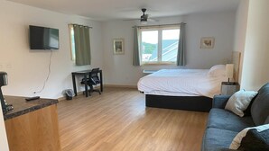 Une chambre à coucher avec un lit, un bureau, une chaise, un téléviseur et une fenêtre avec des rideaux.