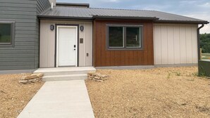 Une maison moderne à deux étages, avec un revêtement extérieur gris, une porte d’entrée blanche et un petit porche en bois.
