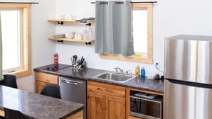 A modern kitchen with wooden cabinets, a stainless steel refrigerator, a built-in oven, and a window with a grey curtain.