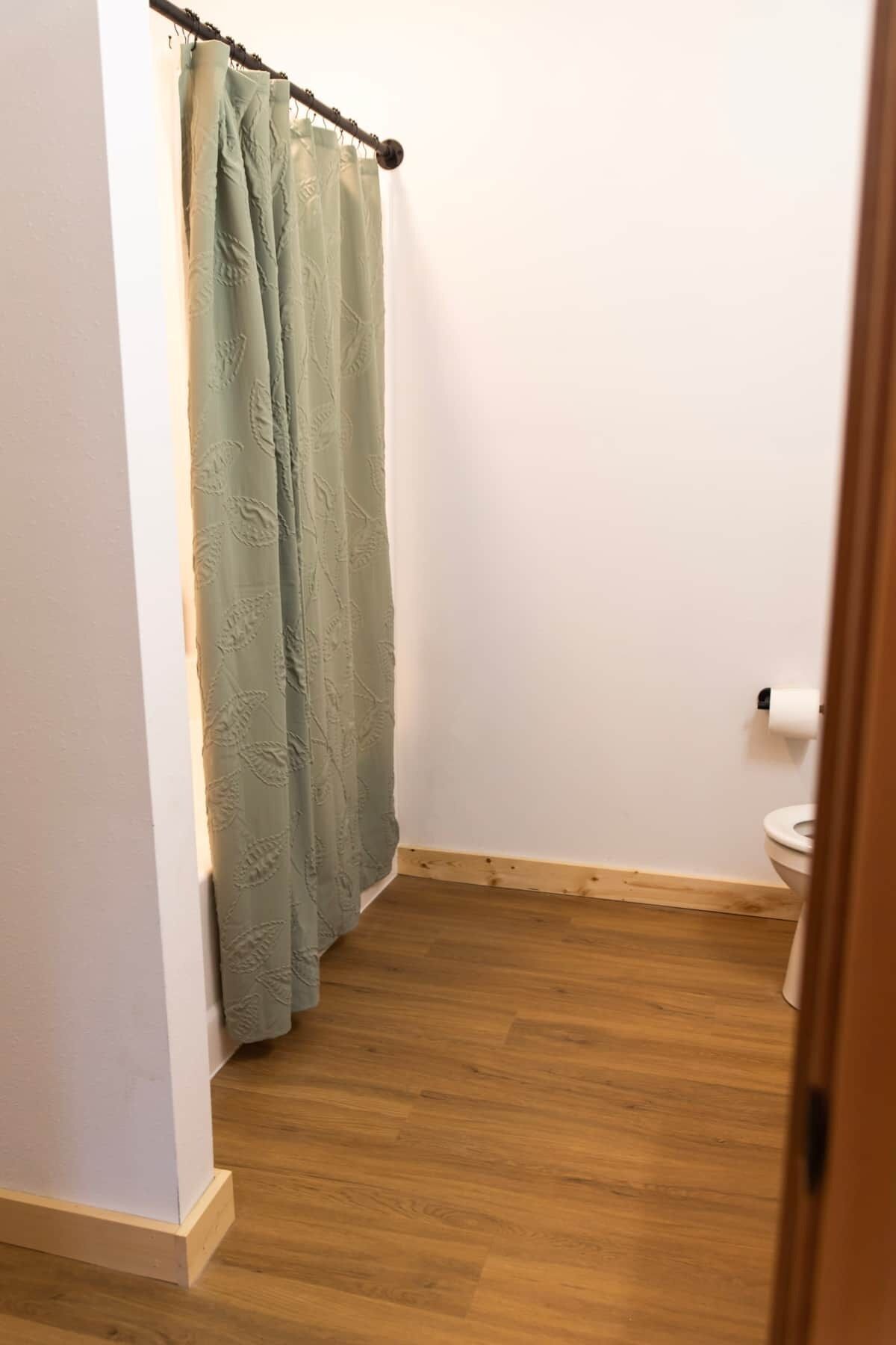 Une petite salle de bain avec un plancher en bois, un rideau de douche vert et des toilettes.