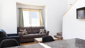 A modern living room with a brown sofa, two black chairs, a small wooden table, and a TV mounted on the wall.