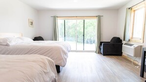 Ein Schlafzimmer mit zwei Betten, einem Sessel, einem Fenster mit Vorhängen und einer Klimaanlage.