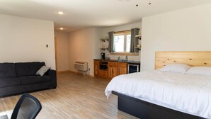 Une chambre avec un lit, un canapé noir, un bureau en bois et un coin cuisine.
