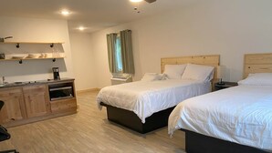 Ein Schlafzimmer mit zwei Betten, einem Holztisch, einer Küchenzeile und einem Fenster mit Vorhängen.