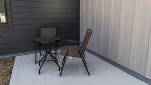 Eine Terrasse mit einem runden Tisch, zwei Stühlen, einem kleinen Tisch und einem Fenster.