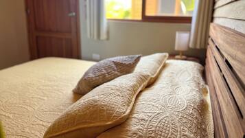 A bed with a patterned bedspread and two pillows, a wooden headboard, and a window with a view of greenery.