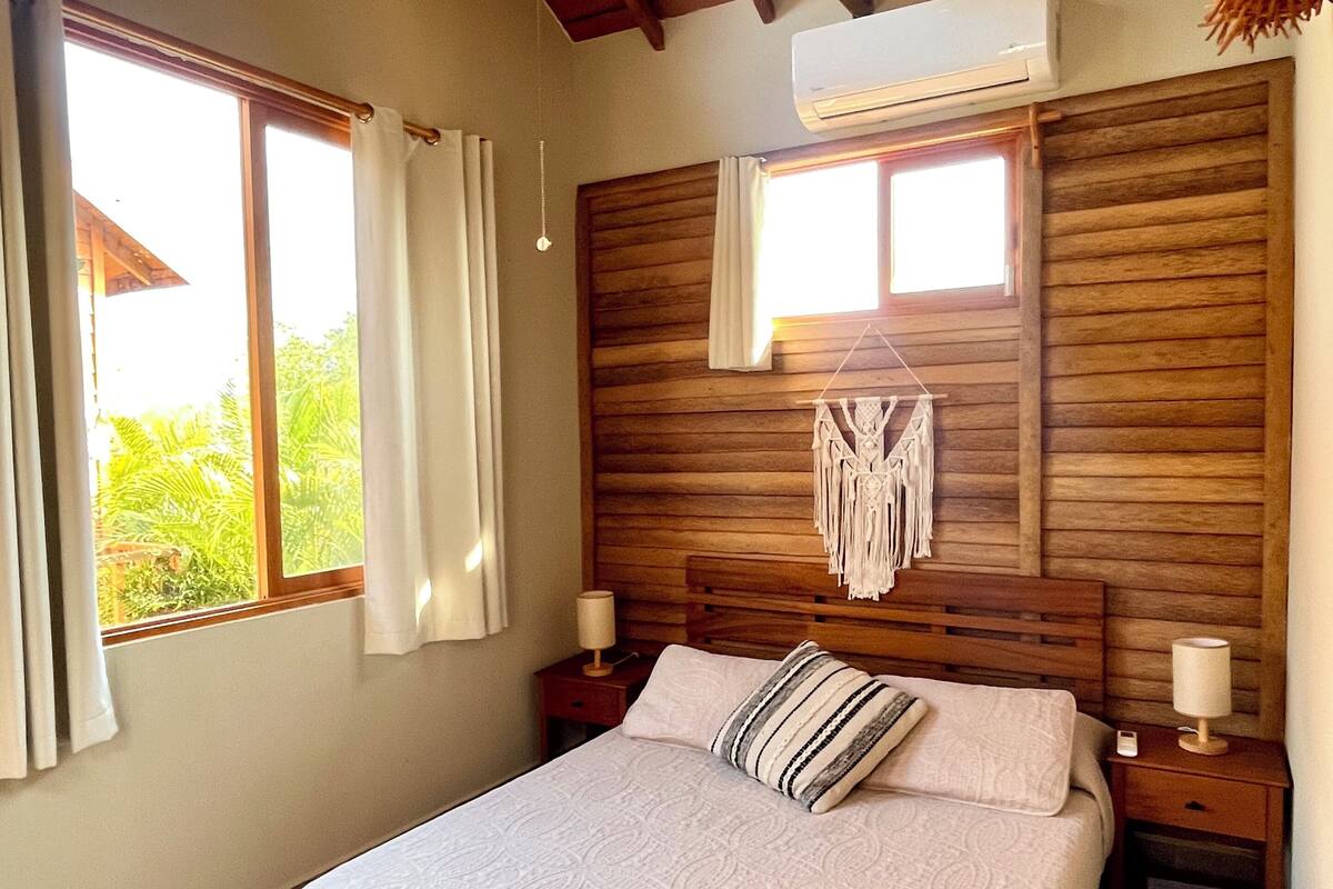 A bedroom with a wooden headboard, a bed with a patterned bedspread, two bedside tables with lamps, and a ceiling fan.
