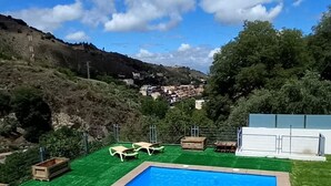 Una piscina rectangular con superficie de agua azul cristalina, rodeada por un césped cuidado y algunas sillas de descanso.