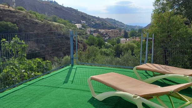 Dos tumbonas en un área de césped artificial verde, con vistas a un pueblo en la ladera.