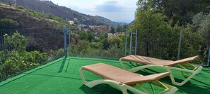 Deux chaises longues sur une pelouse artificielle verte, avec vue sur une ville située sur une colline.