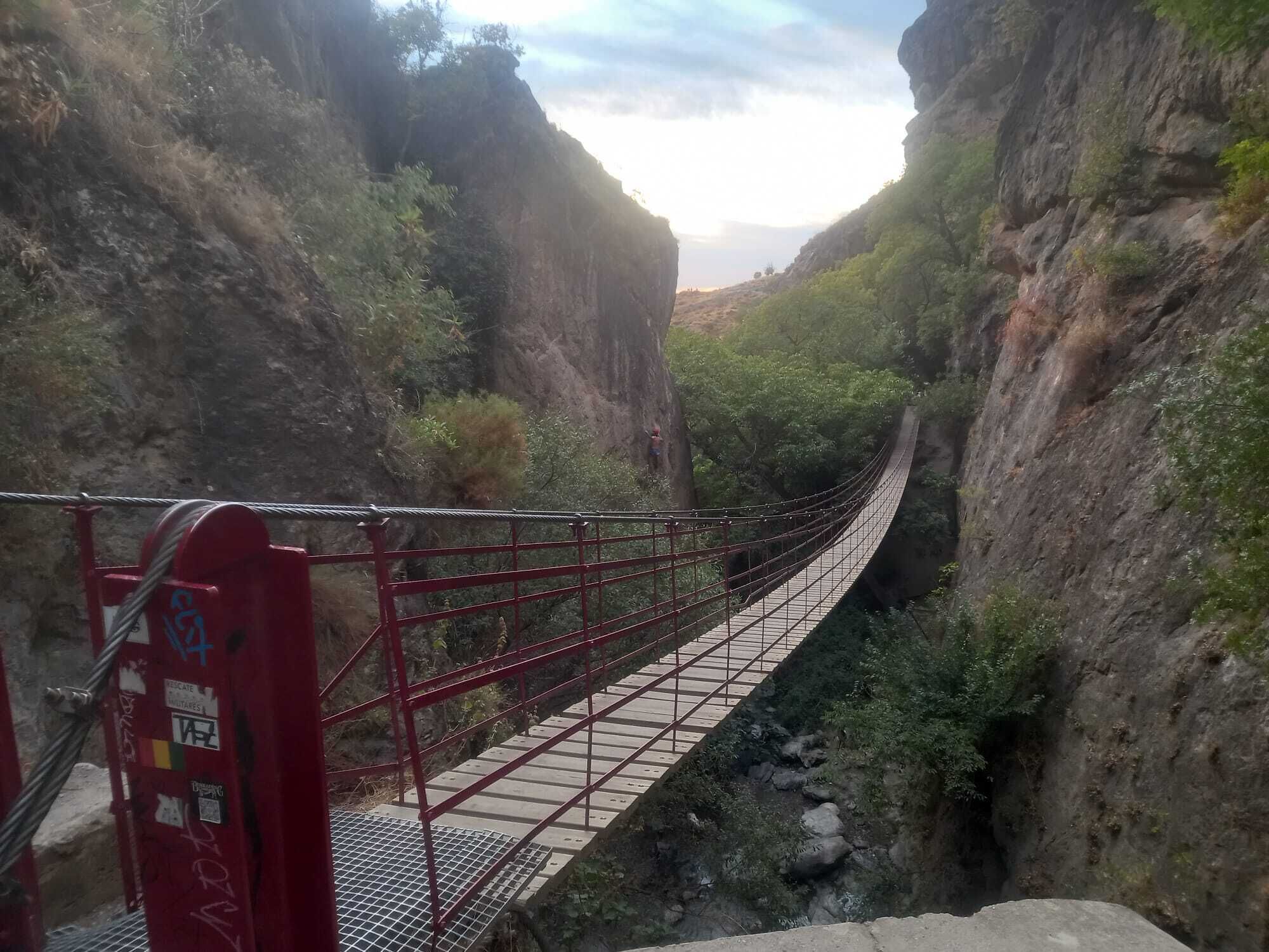 A suspension bridge in a canyon with rocky cliffs and sparse vegetation.
