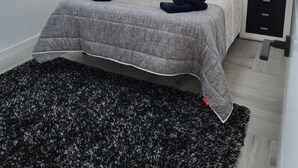 Un dormitorio con cama, dos mesitas de noche, un cuadro colgado en la pared y un tapete blanco y negro.