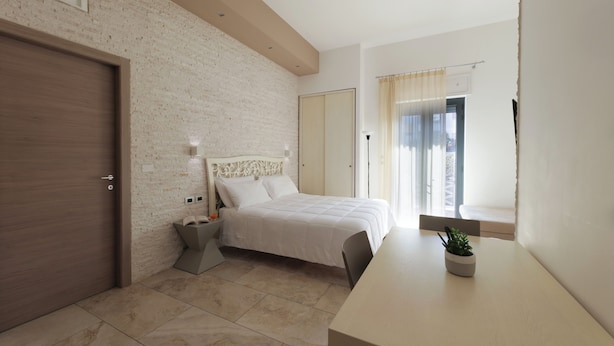 A bedroom with a bed, a bedside table with a lamp, a small plant, a window with curtains, and a brick wall. - Independent apartments/rooms  (Otranto)