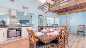 Une cuisine spacieuse dotée d’appareils électroménagers modernes, un coin repas avec des meubles en bois et un étage supérieur aménagé en loft avec balcon.