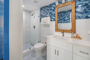 A bathroom with a glass shower enclosure, a toilet, a sink with a mirror, and a patterned wall. - Custom House Inn (Key West)