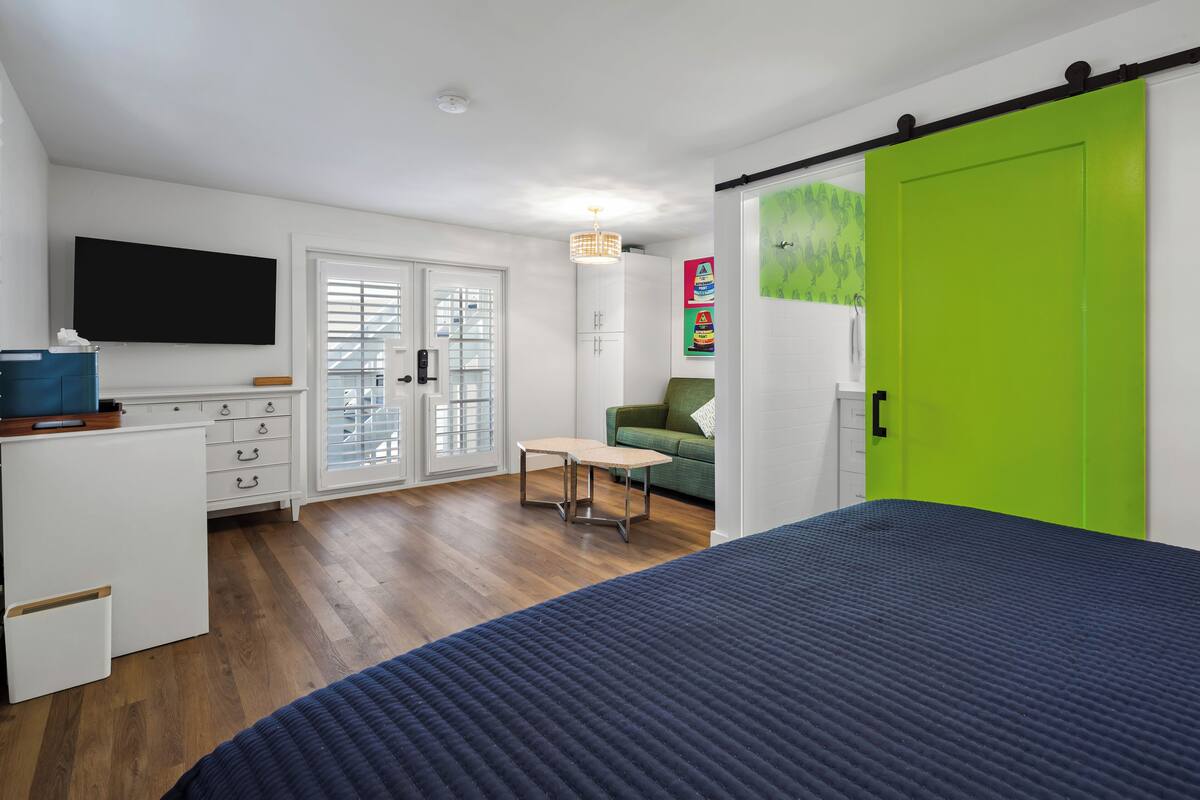 Une chambre moderne avec un lit, un bureau, une chaise, une télévision et une armoire verte.