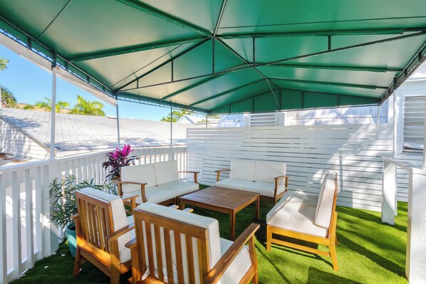 An outdoor patio with a green canopy, wooden furniture, and a white fence. - Custom House Inn (Key West)